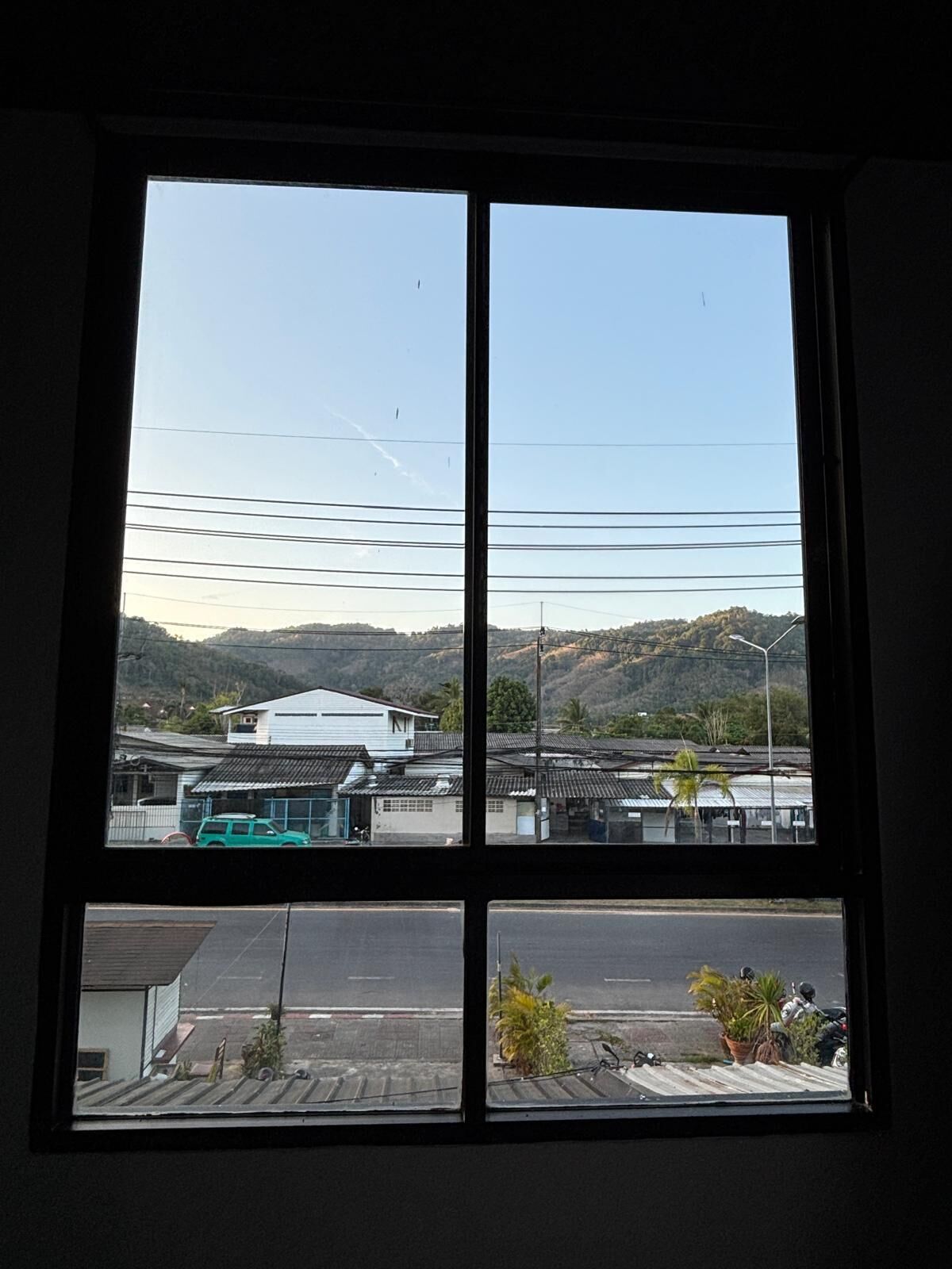 Janela com vista para um edifício, uma estrada e colinas ao fundo.