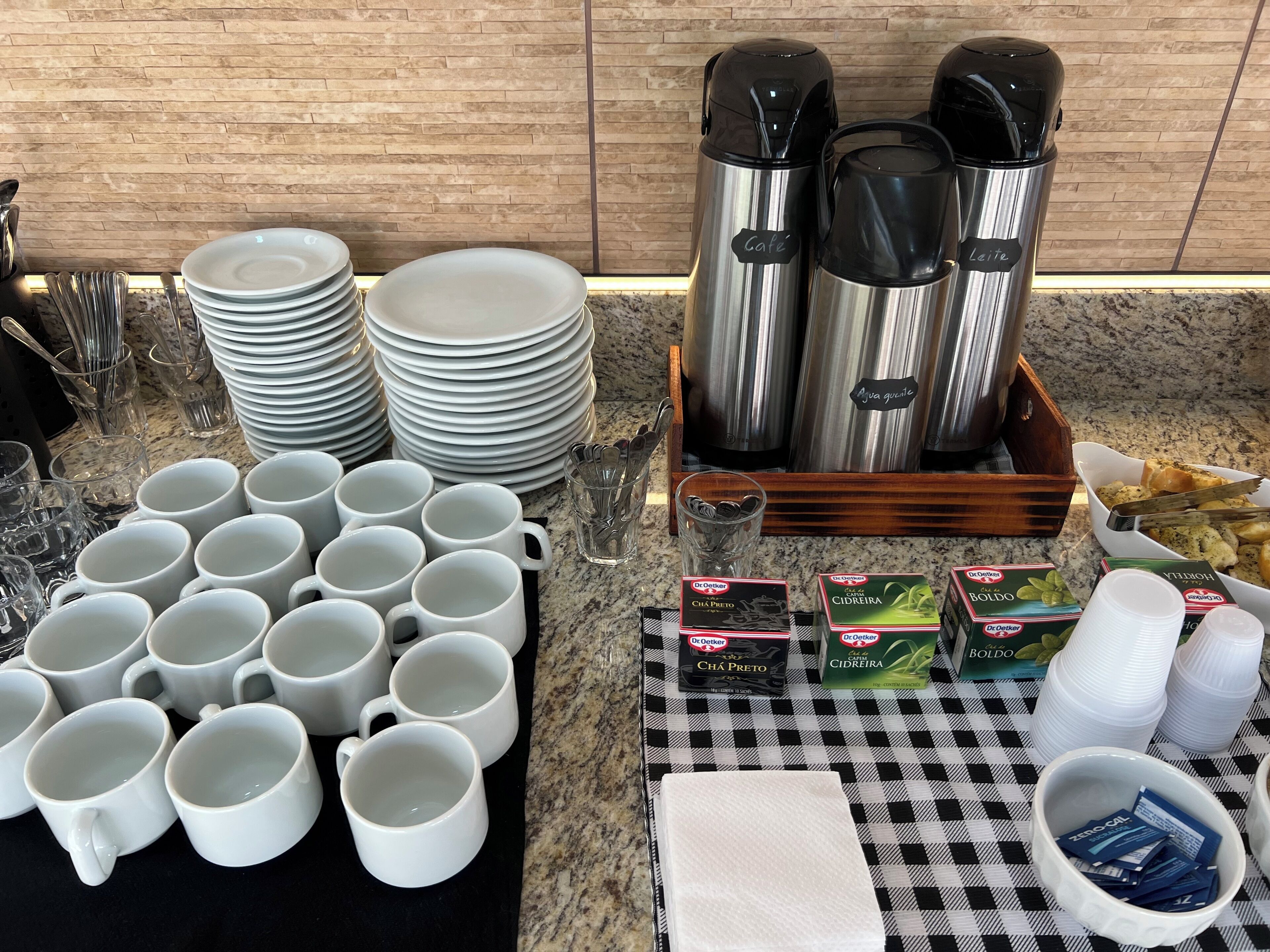 A breakfast buffet setup with stacked plates, mugs, and various breakfast items.
