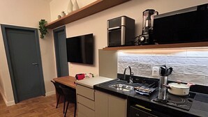 A compact kitchen with a built-in oven, microwave, and coffee maker on a shelf. There is a sink with a faucet, a stovetop, and a dishwasher. The floor is wooden, and there is a door and a chair visible. - 2 quartos 650m praia de Ipanema (Rio de Janeiro)