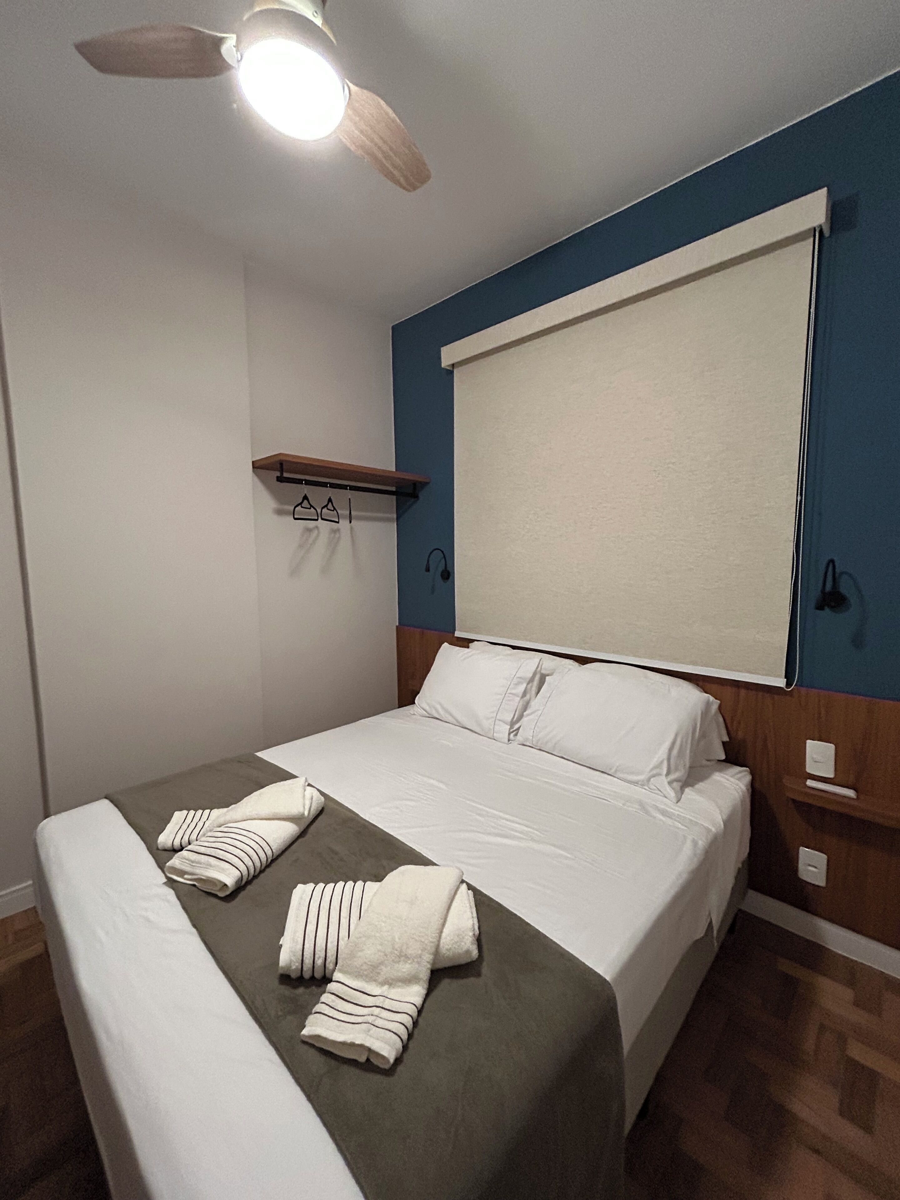 Una cama bien hecha con sábanas blancas, un cabecero de madera y un ventilador de techo.