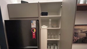 A compact kitchen with a black refrigerator, a white cabinet with shelves, and a grey sofa in the background. - 2 quartos 650m praia de Ipanema (Rio de Janeiro)