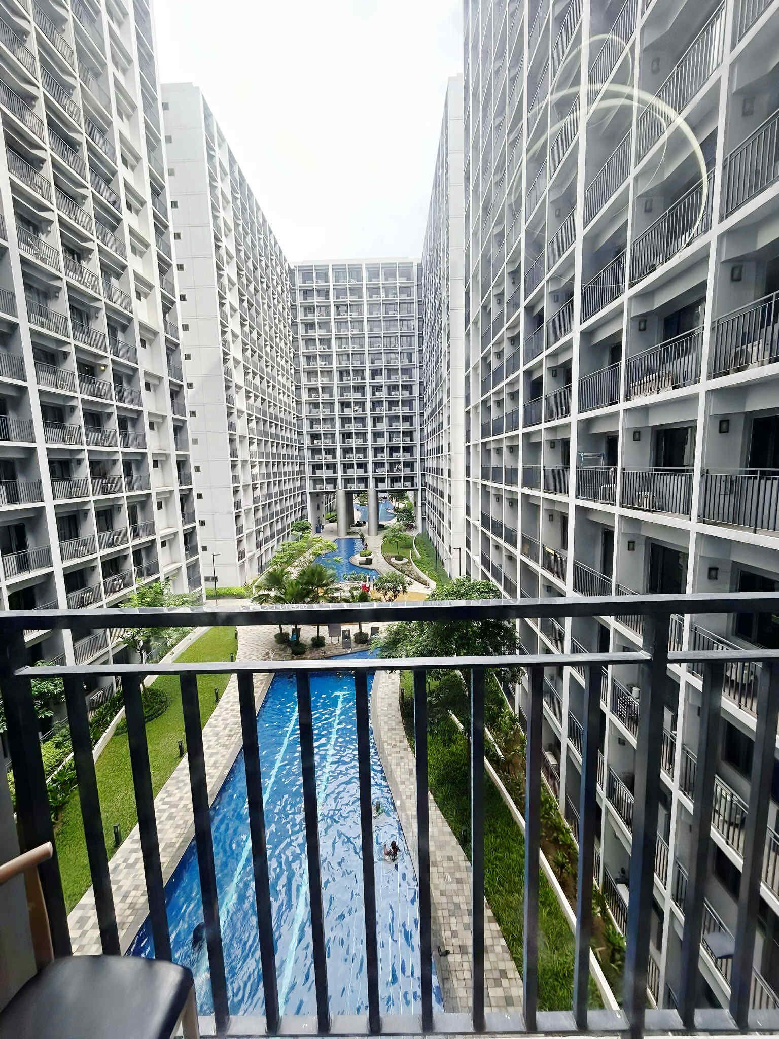 Un immeuble résidentiel de grande hauteur doté de nombreux balcons, d’une cour intérieure avec une piscine et d’un espace verdoyant tout autour.