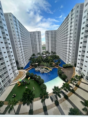 A high-rise residential building with a central courtyard featuring a swimming pool, palm trees, and a playground. - Shore Residences MOA staycation (Pasay)