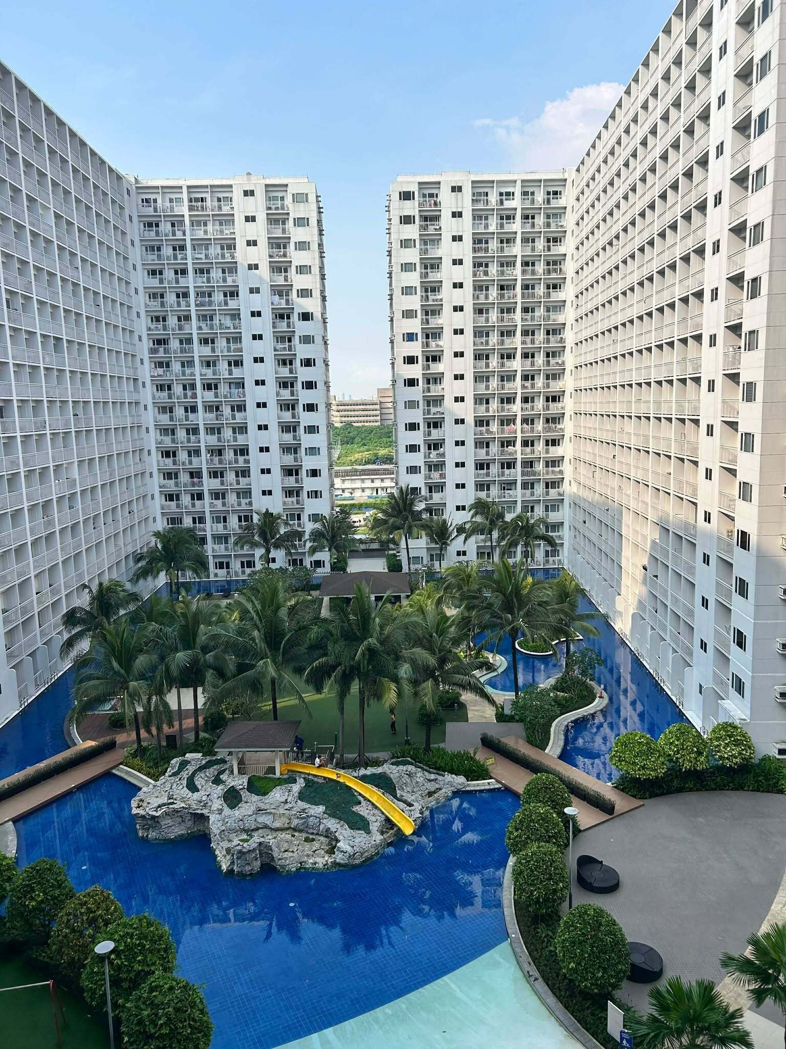 Un hotel de gran altura con una piscina central rodeada de palmeras y una formación rocosa.