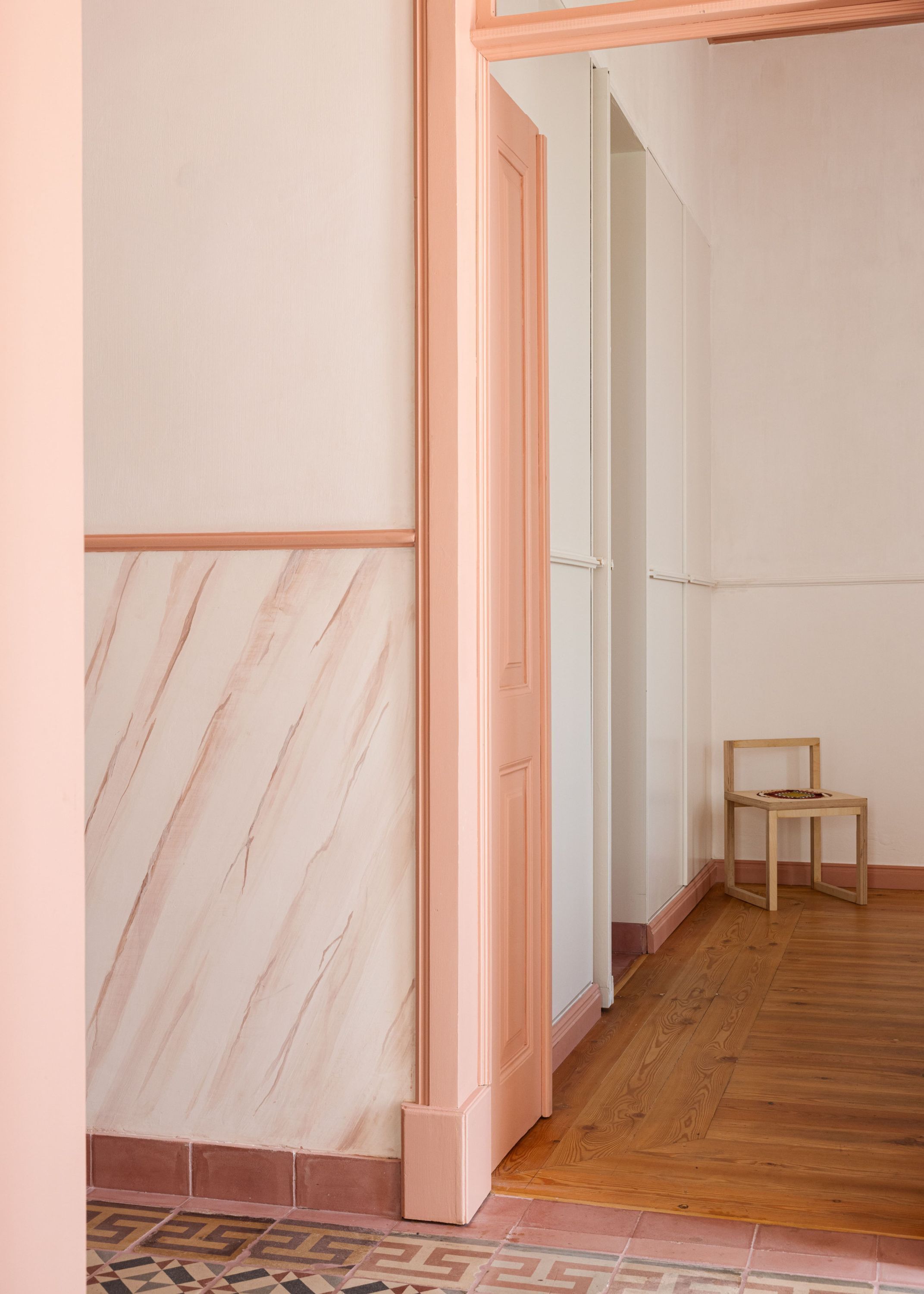 Un couloir avec un plancher en bois, une chaise et une porte donnant sur une autre pièce.
