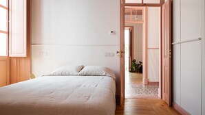 Une chambre avec un lit, une porte donnant sur un couloir et une petite plante posée sur le sol.