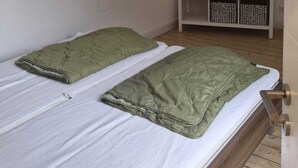 Et værelse med to enkeltsenge, en hvid væg med en enkel tegning, en hvid hylde med en lampe og en dør med en messinggreb.