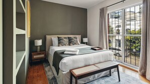 A modern bedroom with a large bed, bedside tables, a bench, and a view of the street through a large window. - Saltillo Condesa House (Ciudad de México)