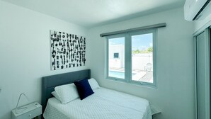 Een slaapkamer met een bed, een nachtkastje, een kunstwerk aan de muur en een raam met uitzicht.