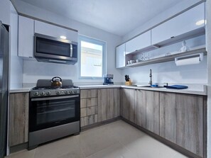 A modern kitchen with a gas stove, oven, microwave, and wooden cabinets. - ARIES APARTMENT (Hatillo)
