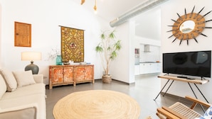 Ein Wohnzimmer mit Sofa, einem runden Teppich, einem Fernseher auf einem Holzschrank, einem Zier-Spiegel und einem Blumentopf.