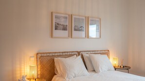Ein ordentlich bezogenes Bett mit weißen Leinen, einem Rattan-Kopfstück und zwei Nachttischlampen.