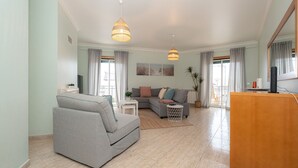 Ein modernes Wohnzimmer mit einem grauen Sofa, einem kleinen Couchtisch und einem Fernsehschrank. Zwei Pendelleuchten hängen von der Decke.