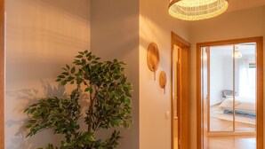 Ein Flur mit einem Blumentopf, einer gewebten Leuchte und einer Holztür, die in ein Schlafzimmer führt.