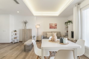Een moderne woonkamer met een eettafel, witte stoelen, een bank en een televisie.