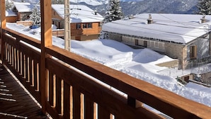 Een houten balkon met uitzicht op besneeuwde huizen en bergen.