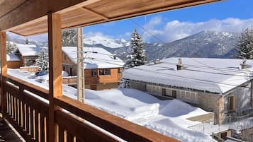 Un balcon en bois offrant une vue sur des maisons et des montagnes enneigées.