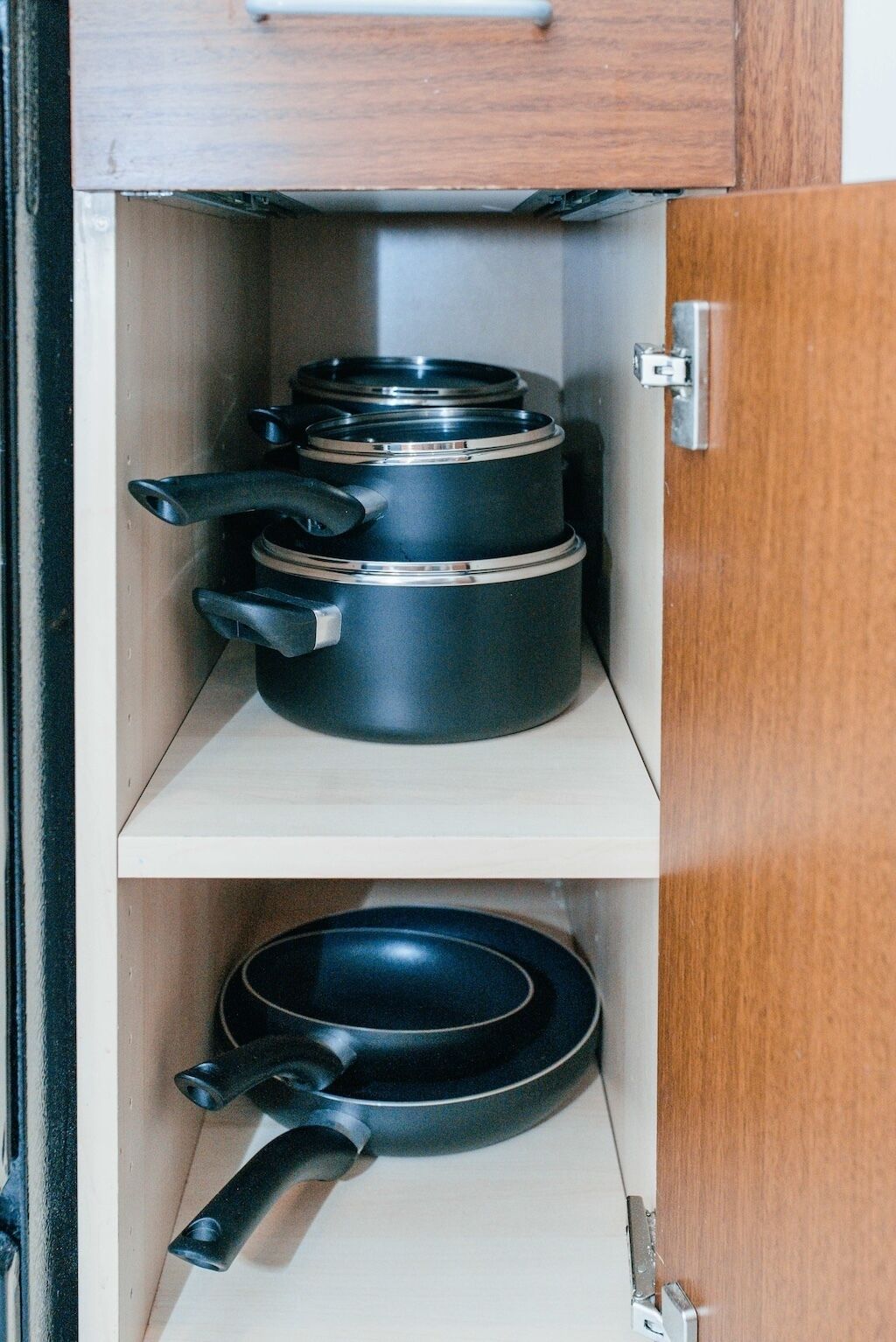 A kitchen cabinet with two shelves, each holding a pot and a pan.