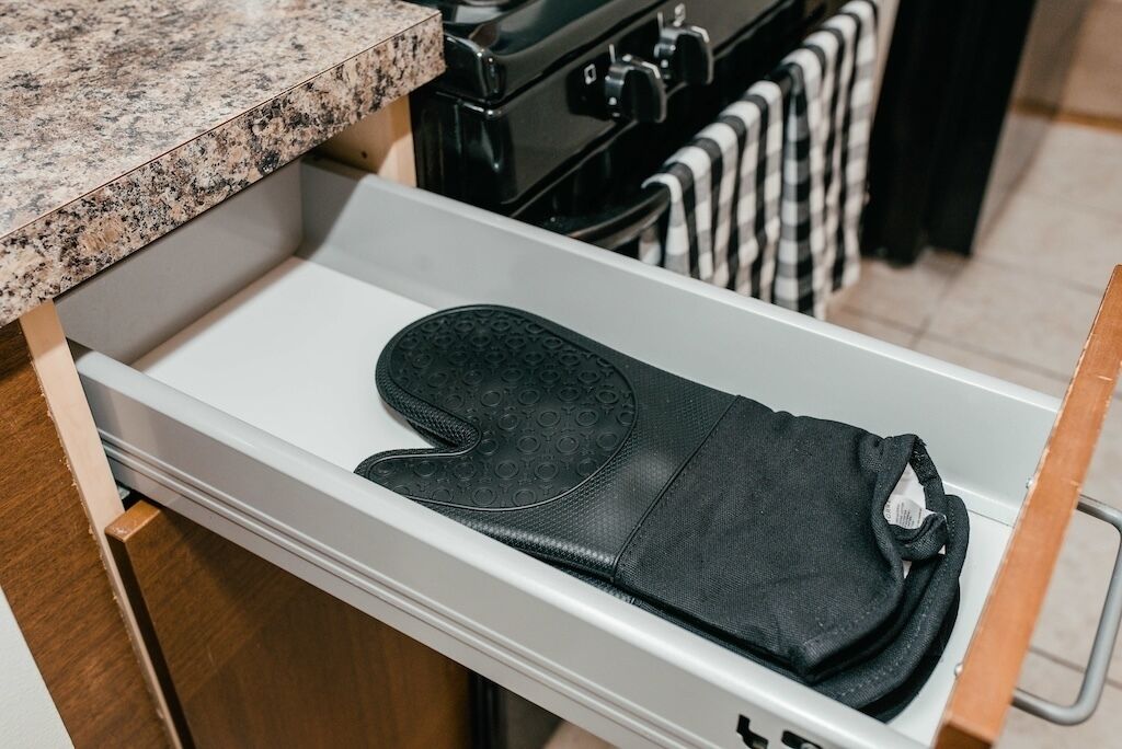 Een keuken met een granieten aanrecht, een kookplaat en een witte lade met een zwarte ovenhandschoen.