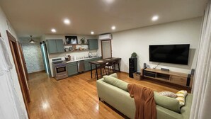 A modern living room with a sofa, TV, and kitchen area with cabinets and appliances.
