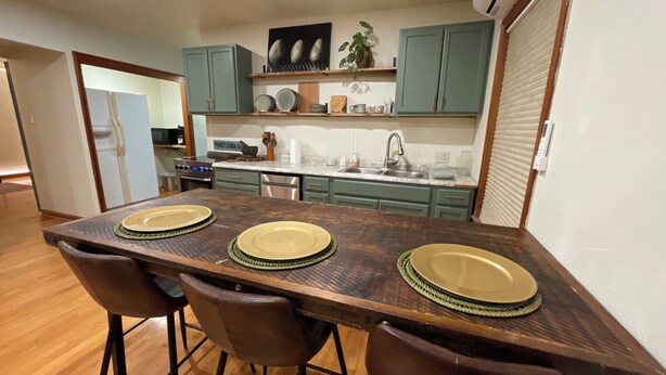 A modern kitchen with teal cabinets, a wooden dining table with four chairs, and a built-in oven.