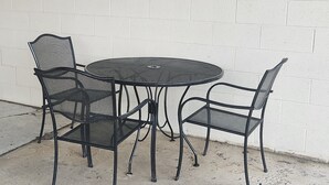A round metal table with four chairs, positioned against a white brick wall. - Cozy 1-bedroom condo in serene Oak Harbor with AC and private dock to Lake Erie (Oak Harbor)