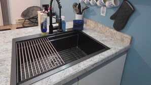 A kitchen with a black sink, white cabinets, and a blue wall. - Cozy 1-bedroom condo in serene Oak Harbor with AC and private dock to Lake Erie (Oak Harbor)