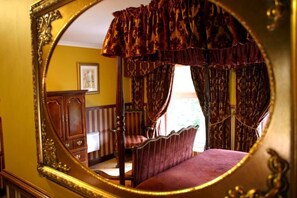 A bedroom with a four-poster bed, a wooden dresser, and a mirror reflecting the room. - Ty Newydd Country Hotel (Hirwaun)