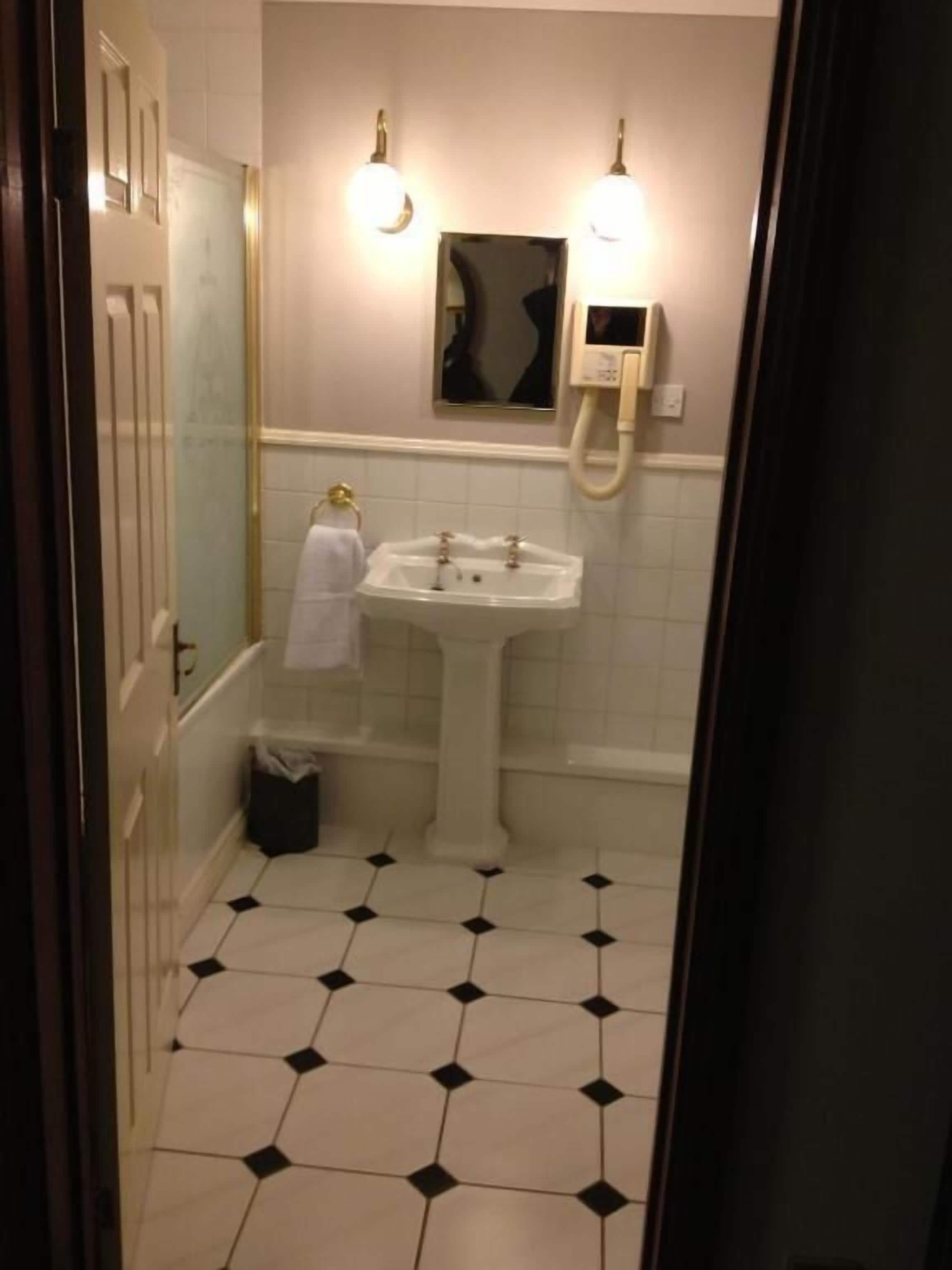 Ein Badezimmer mit einem weißen Waschbecken, einem Spiegel und einer Toilette. Neben dem Waschbecken steht ein Mülleimer.