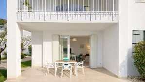 A modern two-story house with a balcony, a patio with a table and chairs, and a view of the interior. - Les Maisons B12 - Carraro Immobiliare Jesolo (Lido di Jesolo)