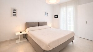 A modern bedroom with a large bed, a bedside table with a lamp, and a wardrobe. - Les Maisons B12 - Carraro Immobiliare Jesolo (Lido di Jesolo)