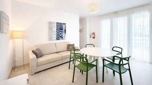 A modern living room with a sofa, a round table, and green chairs. - Les Maisons B12 - Carraro Immobiliare Jesolo (Lido di Jesolo)