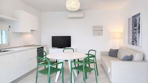 A modern kitchen with white cabinets, a dining table with green chairs, a flat-screen TV, and a white sofa. - Les Maisons B12 - Carraro Immobiliare Jesolo (Lido di Jesolo)