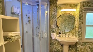 A bathroom with a glass-enclosed shower, a pedestal sink, and a vanity with a mirror. Shelves with towels and toiletries are visible. - Restored Historic Church Retreat in the Catskills (Charlotteville)