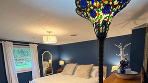 A bedroom with a bed, a nightstand, a dresser, a mirror, and a stained glass lamp. - Restored Historic Church Retreat in the Catskills (Charlotteville)