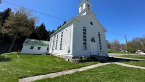 A white church with a steeple, a small adjacent building, and a grassy area with a pathway. - Restored Historic Church Retreat in the Catskills (Charlotteville)