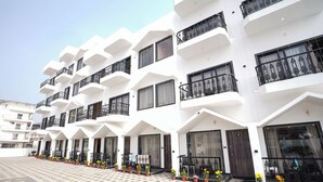 A multi-story hotel with white exterior walls, balconies with black railings, and potted plants along the entrance. - See Pearl (Kanthi)