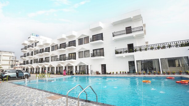 A swimming pool with a tiled deck, a car, and a multi-story building with balconies. - See Pearl (Kanthi)