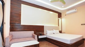 A modern hotel room with a wooden floor, a sofa, a bed, a nightstand, and an air conditioning unit. - See Pearl (Kanthi)