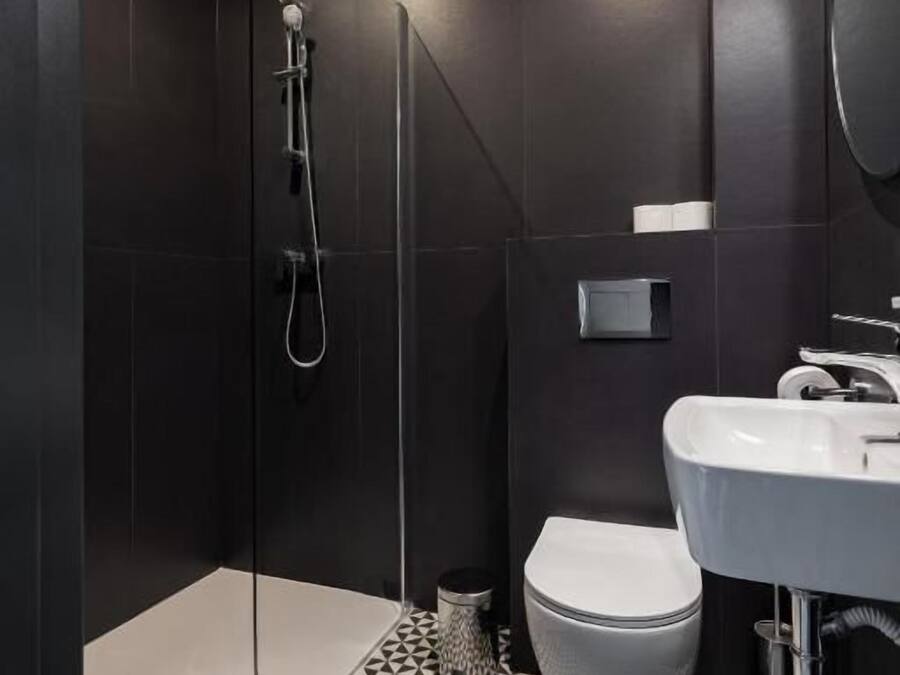 A modern bathroom with a black and white geometric tile floor, a white toilet, and a glass-enclosed shower area.