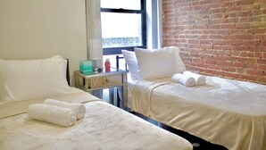 Quarto de hotel com duas camas, uma parede de tijolos e uma janela.