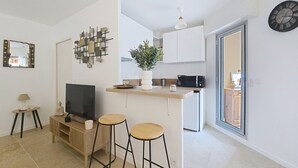 A modern kitchen with a TV, bar stools, a coffee machine, and a potted plant. - Cosy garden-floor studio - Sun & beach on foot (Golfe-Juan)