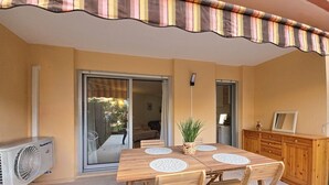 A covered patio with a wooden table and chairs, a potted plant, and a sliding glass door leading to a balcony. - Cosy garden-floor studio - Sun & beach on foot (Golfe-Juan)