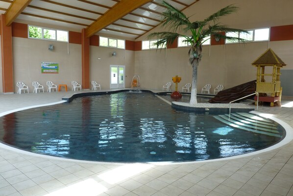 Piscina interna com palmeira, tobogã e um pequeno parquinho.