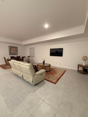 A spacious living room with a beige sofa, a coffee table, and a TV mounted on the wall. - New Construction 4-bedroom House in Marvelous Palm Bay (Palm Bay)
