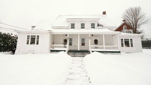 Een wit huis met twee verdiepingen, een veranda, een schoorsteen en een oprit vol sneeuw.