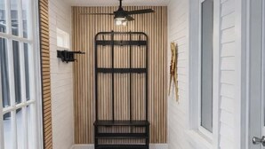 Een kamer met een houten vloer, een plafondventilator, een zwarte metalen bank en een raam met jaloezieën.