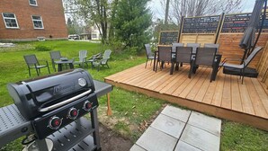 Een achtertuin met een Coleman grill, buitenmeubels en een houten terras.