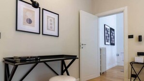 Een gang met een zwarte metalen console tafel, een witte voetenbank en lijstwerken aan de muur.