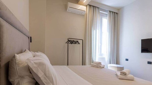 Een hotelkamer met een bed, een televisie, een raam met gordijnen en een handdoekrek.